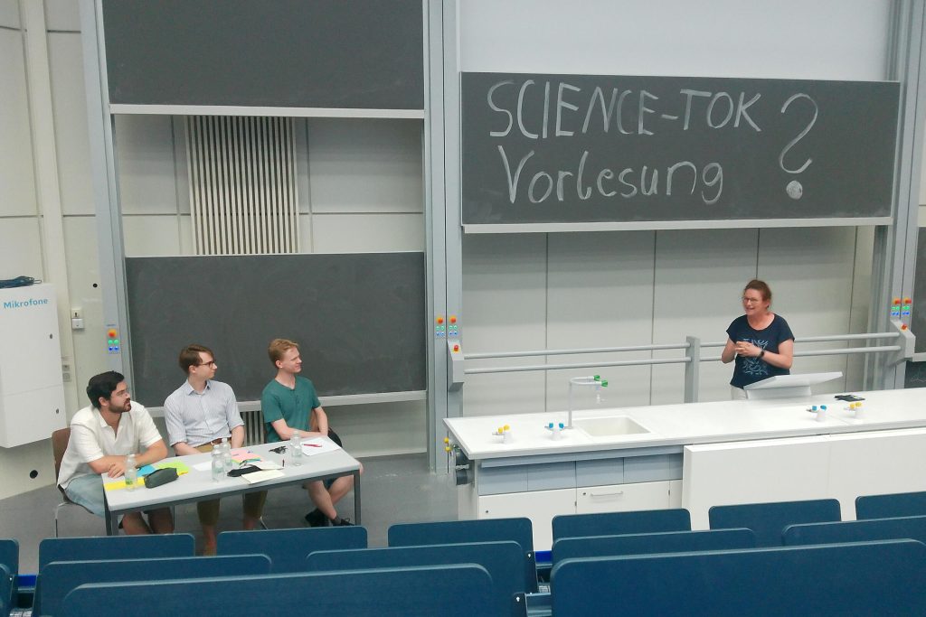 Daniela Czernochowski steht am Rednerpult und fasst dem Team der Studis zugewandt die Debatte zusammen.