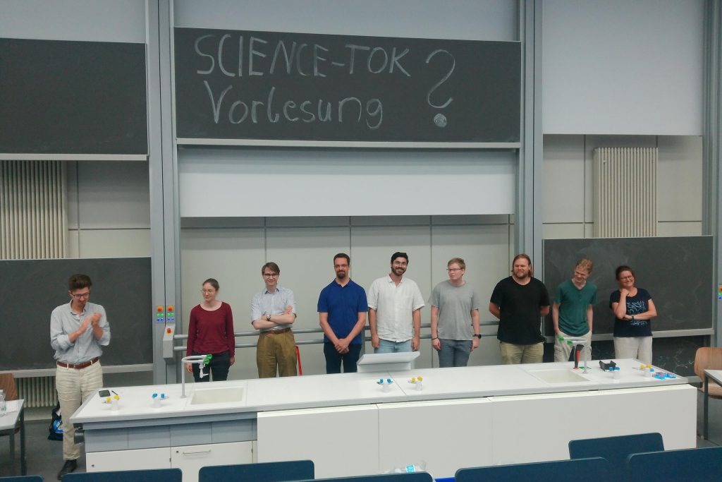 Alle Debattenteilnehmenden und der Moderator stehen nebeneinander zwischen Tafel und Lehrerpult zur Entscheidung des Publikumspreises